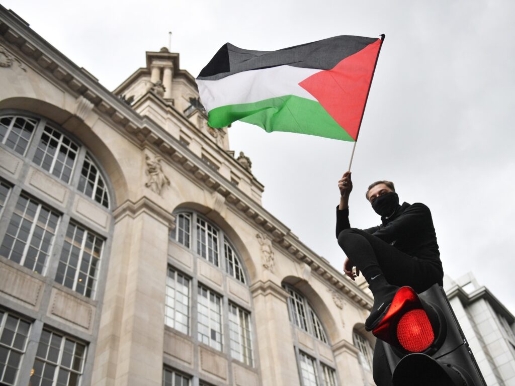 A demonstrator waves a Palestinian flag whilst sat atop a traffic light in London, during a march in solidarity with the people of Palestine amid the ongoing conflict with Israel. Picture date: Saturday May 15, 2021. (Photo by Dominic Lipinski/PA Images via Getty Images)