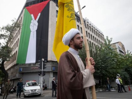 An Iranian cleric holds a yellow flag while standing next to a giant Palestinian flag duri