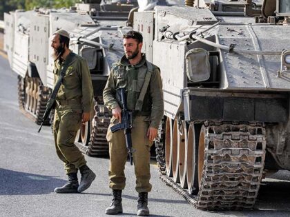 Israeli army soldiers walk before tracked vehicles deployed at a position in the Upper Gal