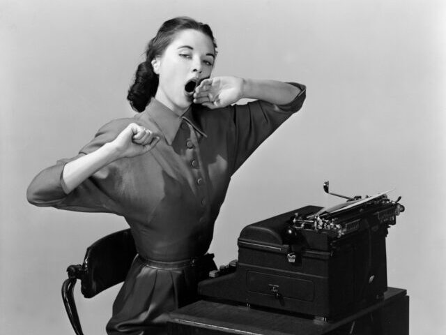 ENGLAND - AUGUST 07: A photograph of a woman sitting yawning at a typewriter, taken by Ph