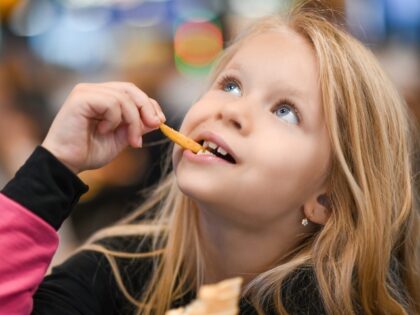 Little girl eating french fries in fast food cafe.