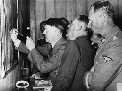 Adolf Hitler (m) marks a spot on a map, which hangs on a wall in the Führer headquarters