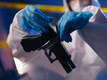 Close-up of criminologist in protective suit putting a gun in a plastic bag at the crime s