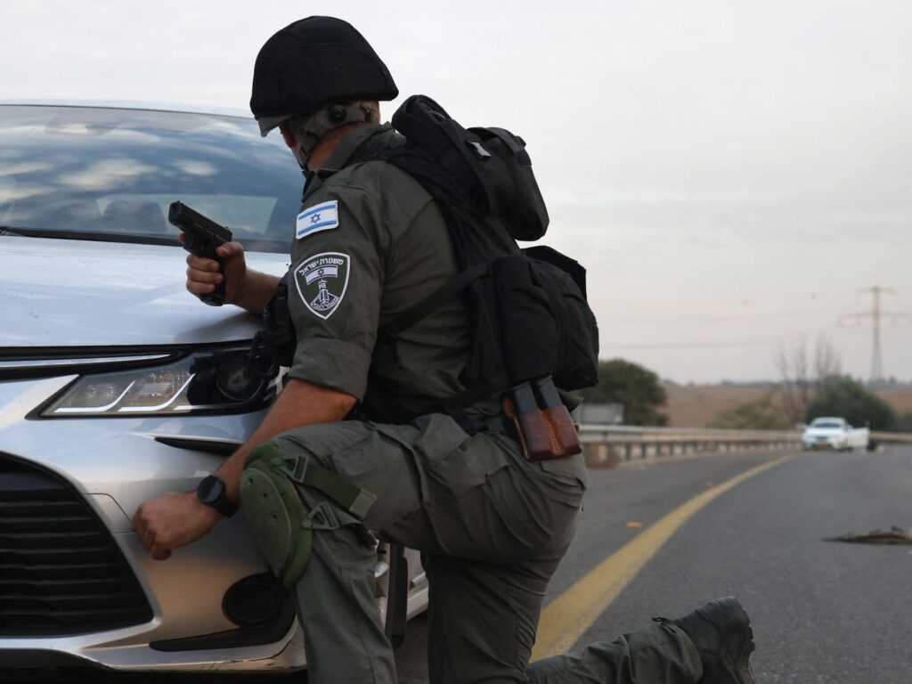 EDITORS NOTE: Graphic content / An Israeli soldiers take cover behind a car as he looks toward bodies on a main road near the Gevim Kibbutz, close to the border with Gaza on October 7, 2023. Palestinian militants have begun a "war" against Israel which they infiltrated by air, sea and land from the blockaded Gaza Strip, Israeli officials said, a major escalation in the Israeli-Palestinian conflict. (Photo by Oren ZIV / AFP) (Photo by OREN ZIV/AFP via Getty Images)