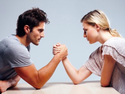 Profile view of a young couple arm wrestling against grey background