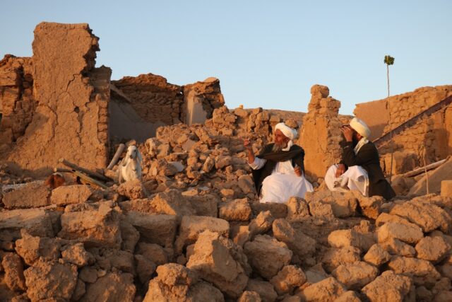 Afghan men sit in the rubble of their flattened homes in Sarbuland village in Herat provin