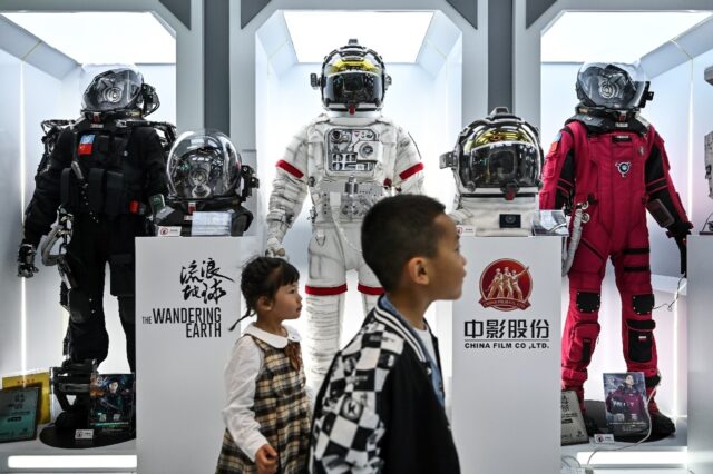 Children walk past space suits from the Chinese sci-fi movie "The Wandering Earth" on disp