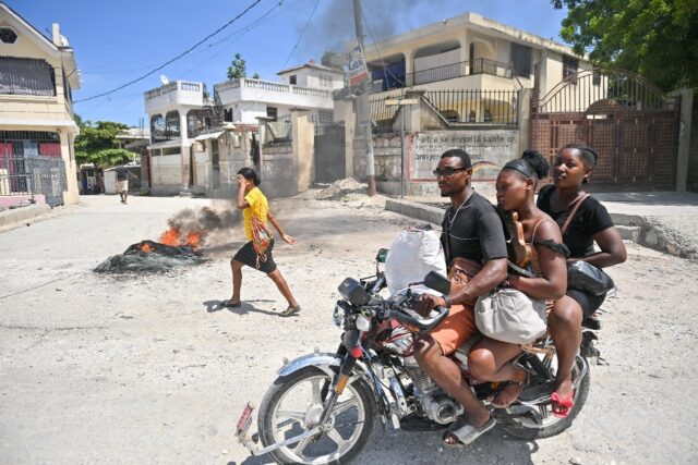 A motorcyclist passes by burning tires as people demonstrate over the rise in the cost of