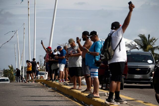 People desperately try to find a signal to use their mobile phones after Hurricane Otis sl