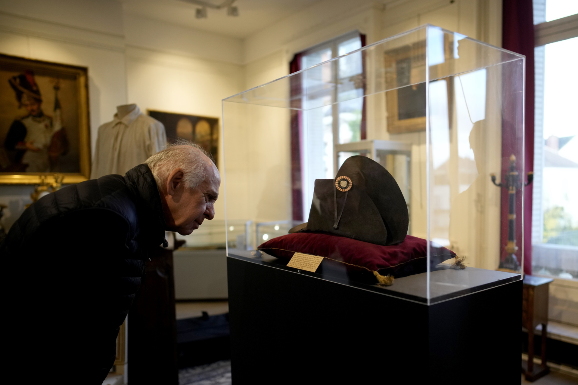 A visitor watches one of the signature broad, black hats that Napoléon wore when he ruled 19th century France and waged war in Europe on display at Osenat's auction house in Fontainebleau, south of Paris, Friday, Nov. 17, 2023. The hat is tipped to fetch more than half a million euros (dollars) at the auction Sunday of Napoleonic memorabilia patiently collected by a French industrialist. (AP Photo/Christophe Ena)
