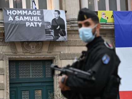 A French police officer stands next to a portrait of French teacher Samuel Paty on display on the facade of the Opera Comedie in Montpellier on October 21, 2020, during a national homage to the teacher who was beheaded for showing cartoons of the Prophet Mohamed in his civics class. …