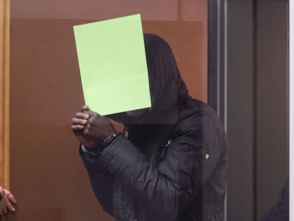 Gambian defendant Bai L., accused of of crimes against humanity, murder and attempted murder, hides behind a folder as he arrives in the courtroom on April 25, 2022 in Celle, northern Germany, at the opening of his trial. - The suspect, identified by media as Bai L., is accused of …