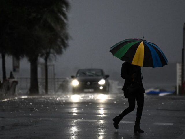 TOPSHOT - A woman holding an umbrella crosses a street under the rain ahead of storm Ciara