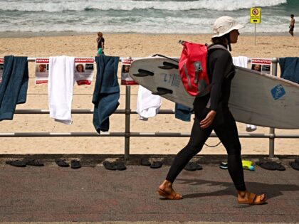 A surfer carrying her board walks past posters, towels and flip-flops that are part of a p