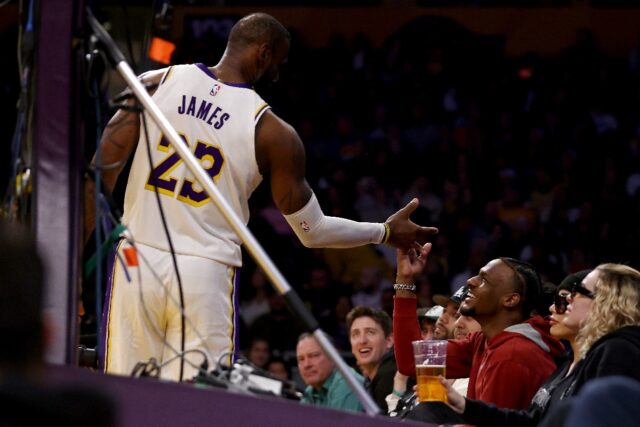 Bronny James, shown at right greeting his father LeBron during an NBA game on November 19,