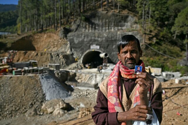 A father stands in front of the entrance to the Silkyara road tunnel, holding up a picture