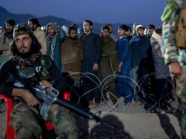 Taliban fighters stand guard as Afghan refugees line up to register in a camp near the Tor