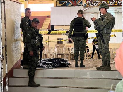 Military personnel stand guard at the entrance of a gymnasium while police investigators (