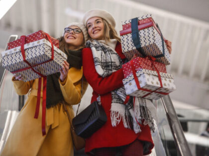Two young women holding bunch of Christmas presents on descending escalator.