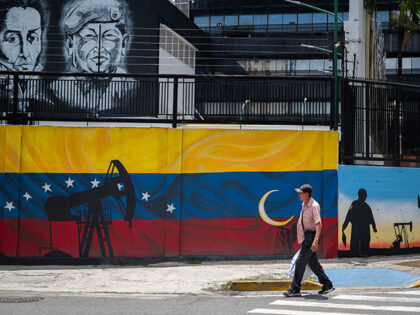 A man walks past a mural painted on the wall outside the headquarters of PDVSA (Petroleros