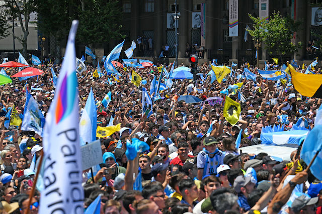 Supporters of Argentina's new president Javier Milei wave national flags as he delivers a speech after swearing in during his inauguration ceremony outside the Congress in Buenos Aires on December 10, 2023. Libertarian economist Javier Milei was sworn in Sunday as Argentina's president, after a resounding election victory fueled by fury over the country's economic crisis. "I swear to God and country... to carry out with loyalty and patriotism the position of President of the Argentine Nation," he said as he took the oath of office, before outgoing President Alberto Fernandez placed the presidental sash over his shoulders. (Photo by LUIS ROBAYO / AFP)