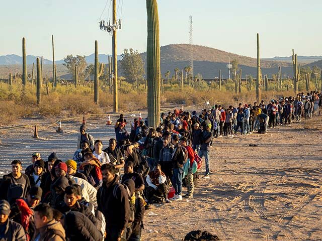 Immigrants line up at a remote U.S. Border Patrol processing center after crossing the U.S.-Mexico border on December 07, 2023 in Lukeville, Arizona. A surge of immigrants illegally passing through openings cut by smugglers in the border wall has overwhelmed U.S. immigration authorities, causing them to shut down several international …