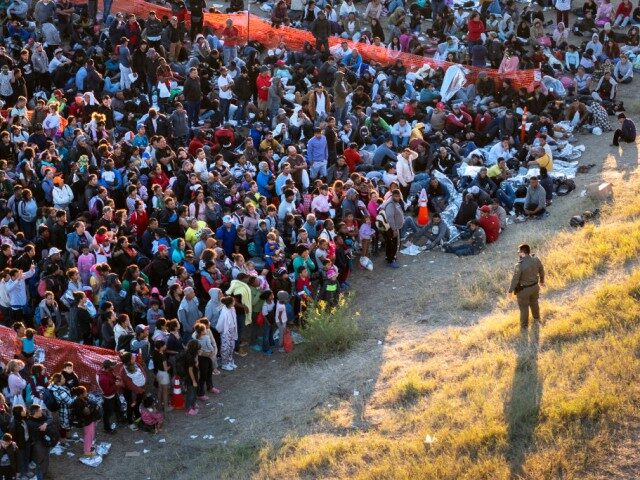 EAGLE PASS, TEXAS - DECEMBER 17: In an aerial view, a U.S. Border Patrol agent watches over migrants waiting to be processed after crossing from Mexico into the United States on December 17, 2023 in Eagle Pass, Texas. A surge of migrants, as many as 12,000 per day, crossing the …