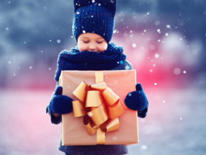 adorable kid with big gift box under a snowfall. Focus on gift box