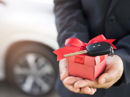 A man's hands are extended in which is a gift box with a car key (Stock photo via Getty).