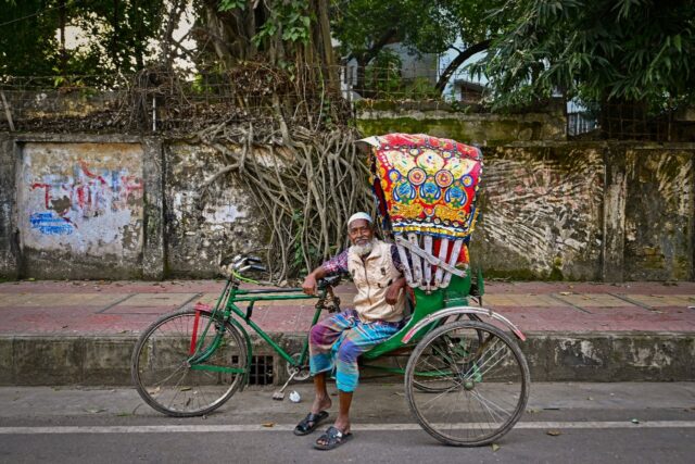 Bicycle rickshaw driver Mohammad Harun poses for a portrait with his vehicle on a street i