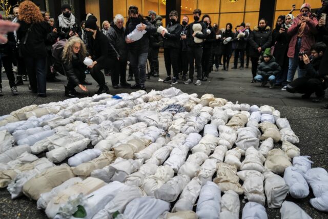 People gather and mourn in front of 500 baby dolls wrapped in a shroud, in remembrance of