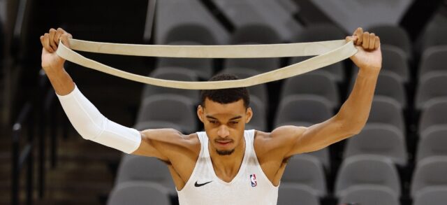 San Antonio Spurs rookie Victor Wembanyama toes through stretching exercises before an NBA