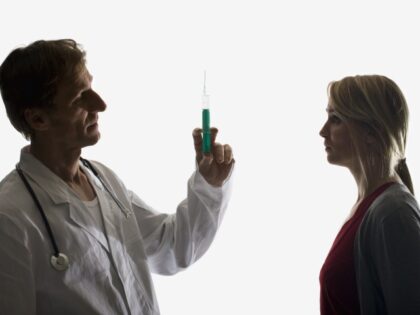A doctor holds up a syringe facing a worried patient
