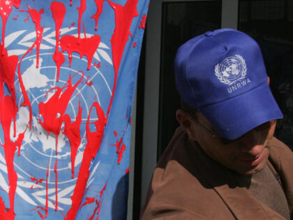 A employee of UN's main agency, UNRWA, stands by a flag covered with red paint during a pr