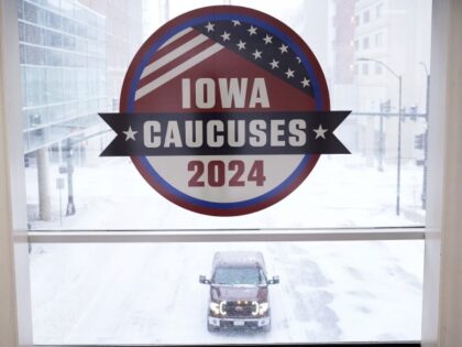 A pickup truck is driven down a snow covered road under an Iowa Caucus sign, Friday, Jan.