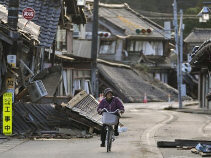 A woman bikes amid damaged houses in Noto town in the Noto peninsula facing the Sea of Jap