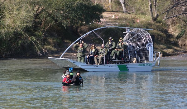 A migrant family crosses the Rio Grande as a Border Patrol boat carrying Del Rio Sector Acting Chief Patrol Agent Juan Bernal. (Randy Clark/Breitbart Texas)