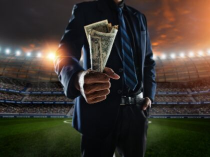 businessman holding large amount of bills at Soccer stadium in background