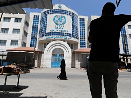 Palestinians walk past the Beach Health Center building of the United Nations Relief and W