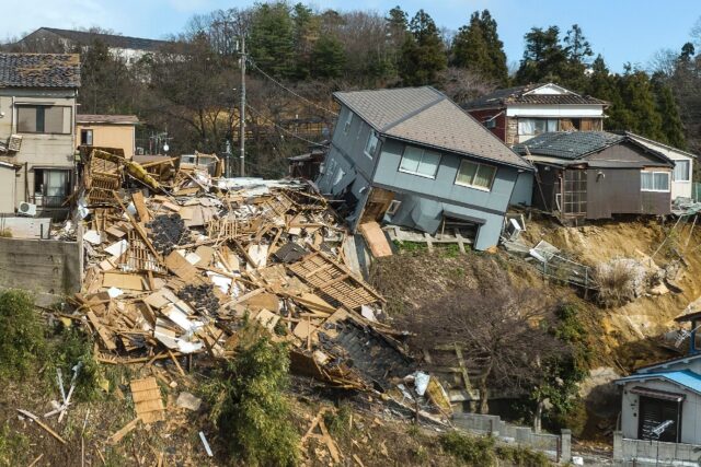 Damaged houses, including one totally collapsed (C), are pictured along a street in Wajima