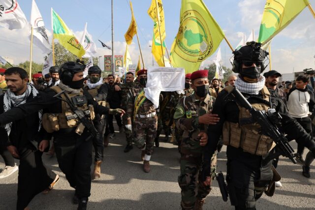 Hundreds of people waving the flags of pro-Iran groups attend the funeral on January 25, 2