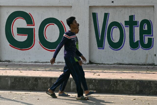 Men walk past a wall writing urging people to vote in Dhaka on January 6, 2024, on the eve
