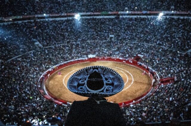 A man wearing a traditional hat watches a bullfight at the Plaza de Toros in Mexico City