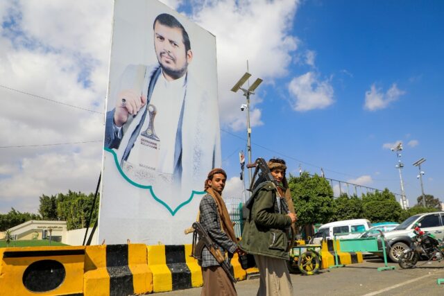 Yemeni fighters walk past a large portrait of Huthi leader Abdulmalik al-Huthi on a street