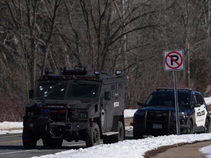 A police vehicle with what appears to be bullet pockmarks on its windshield is parked near