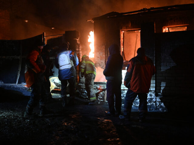 Ukrainian emergency and rescue personnel walk past a burning structure as they work at the