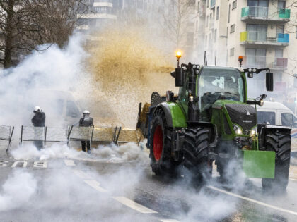 TOPSHOT - A farmer emits hay from his tractor onto Belgian riot police officers as gas ris