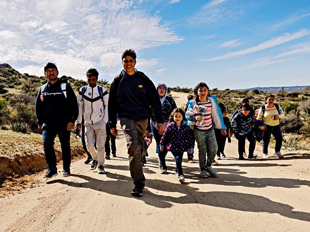 SAN DIEGO, CALIFORNIA - FEBRUARY 23: Migrants walk on a dirt road after crossing the nearb