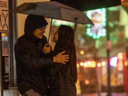 PASADENA, CA - FEBRUARY 4, 2024: A couple share space and an umbrella at a cross walk as h