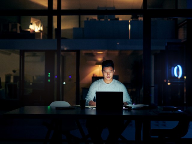 hot of a young businessman using a laptop during a late night in a modern office.